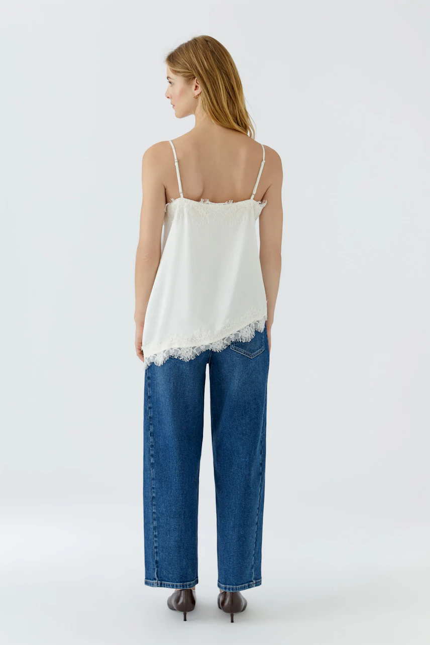 Damen-Top: Frau im weißen Top mit Spitzenbesatz, kombiniert mit blauen Jeans, von hinten gesehen.