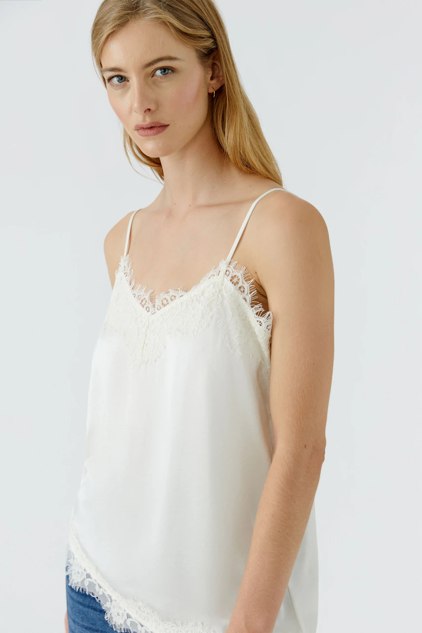 Damen-Top: Frau im weißen Spitzentop mit schmalen Trägern und lässigem Look.