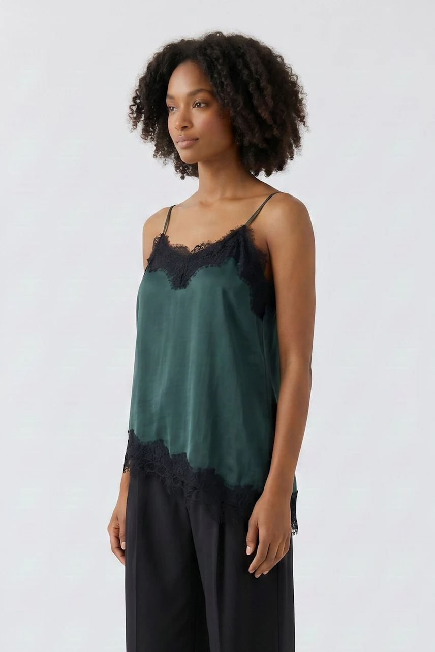 Woman in a green silk top with black lace trim, paired with black pants, standing confidently.