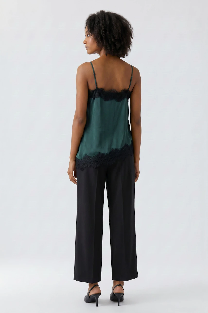 Woman in green lace-trimmed top and black pants, viewed from the back.
