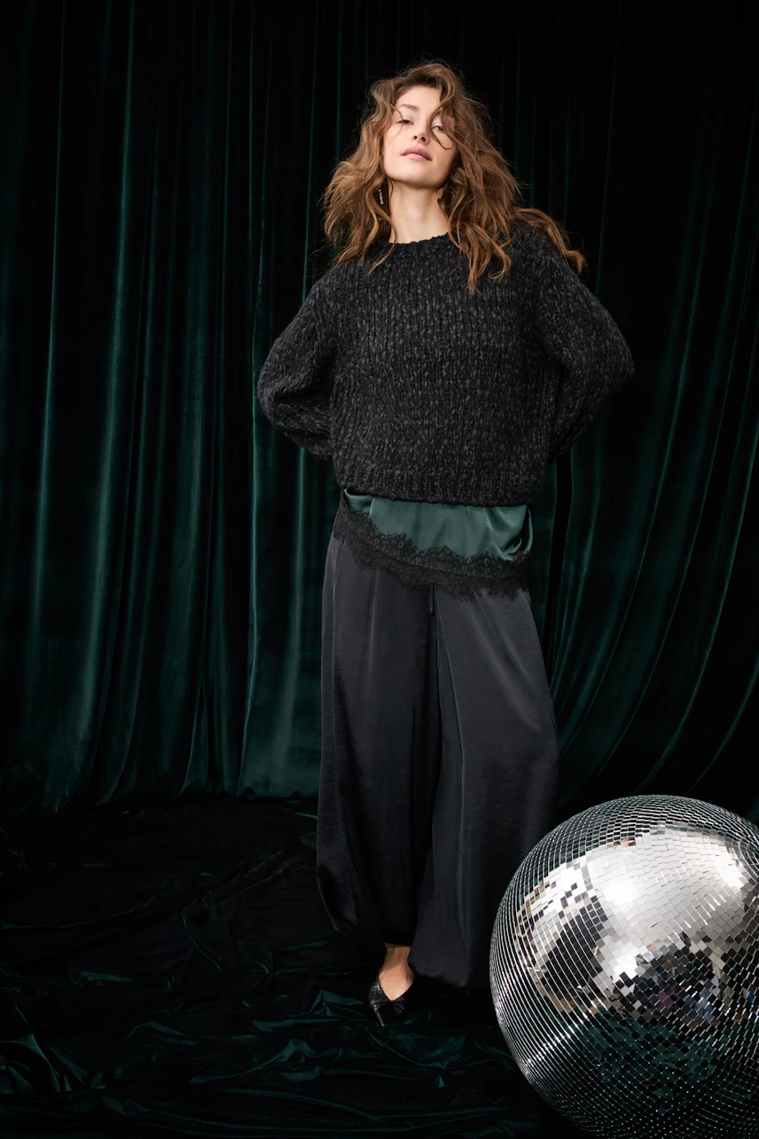 Casual women's top: Woman in a black knit pullover over a green top with lace detail, standing confidently.