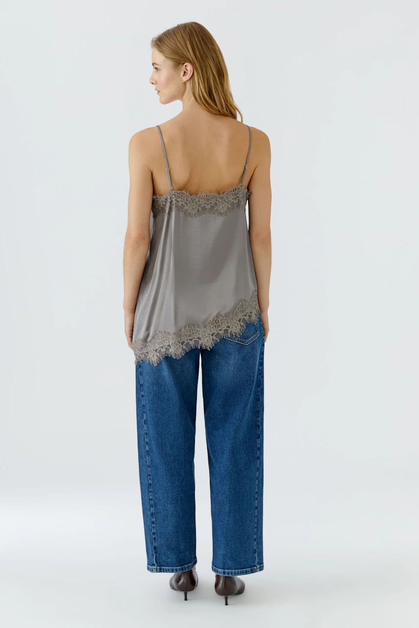 Damen-Top: Frau im grauen Top mit Spitzenbesatz und blauer Jeans, von hinten gesehen.