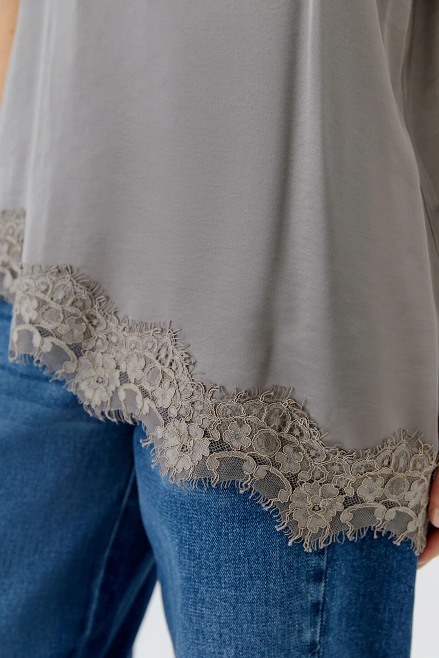Graues Damen-Top mit Spitzenbesatz am Saum, kombiniert mit blauer Jeans. Kein Model sichtbar.