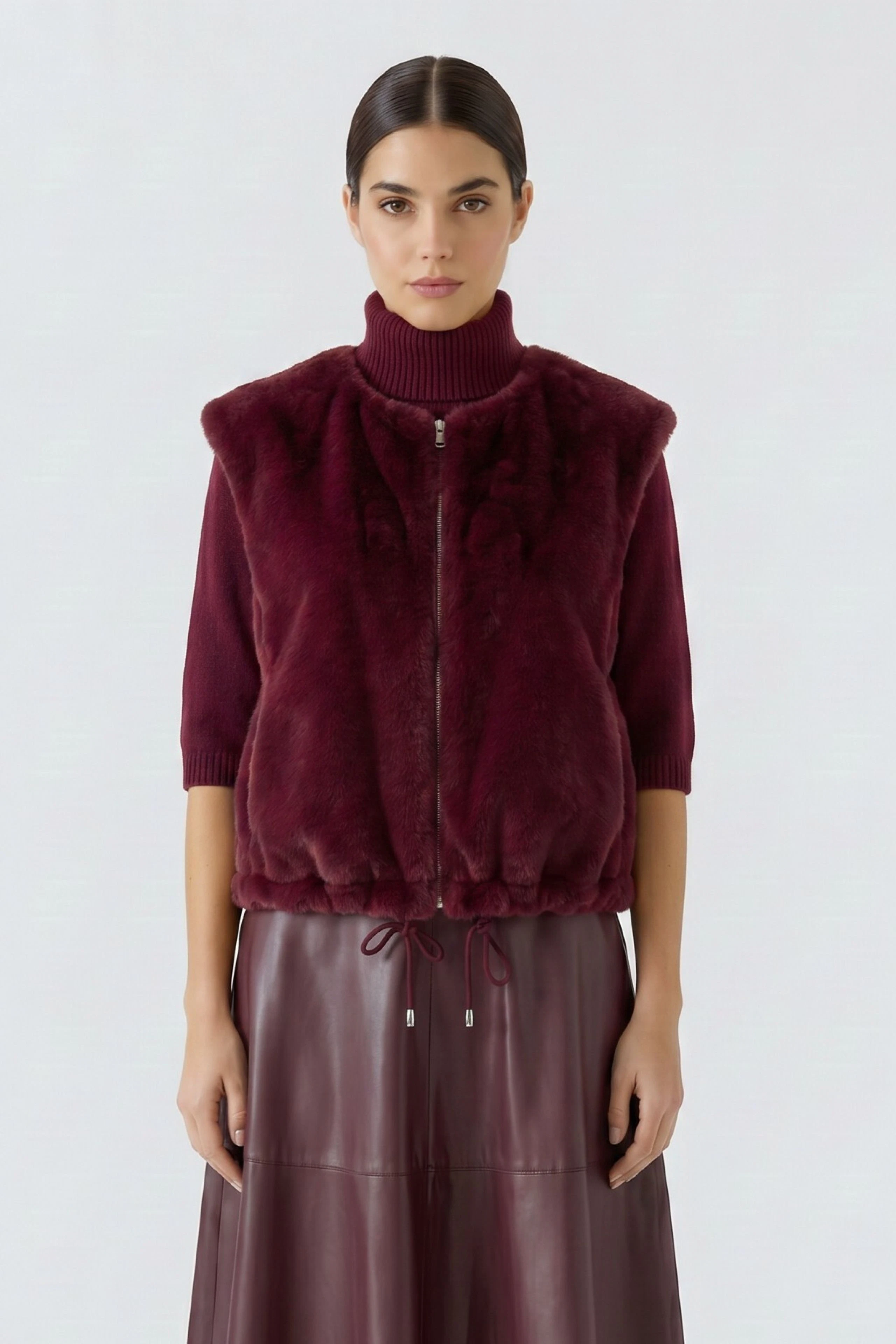 Woman in a burgundy vest with a high-neck sweater and matching skirt, looking confidently ahead.