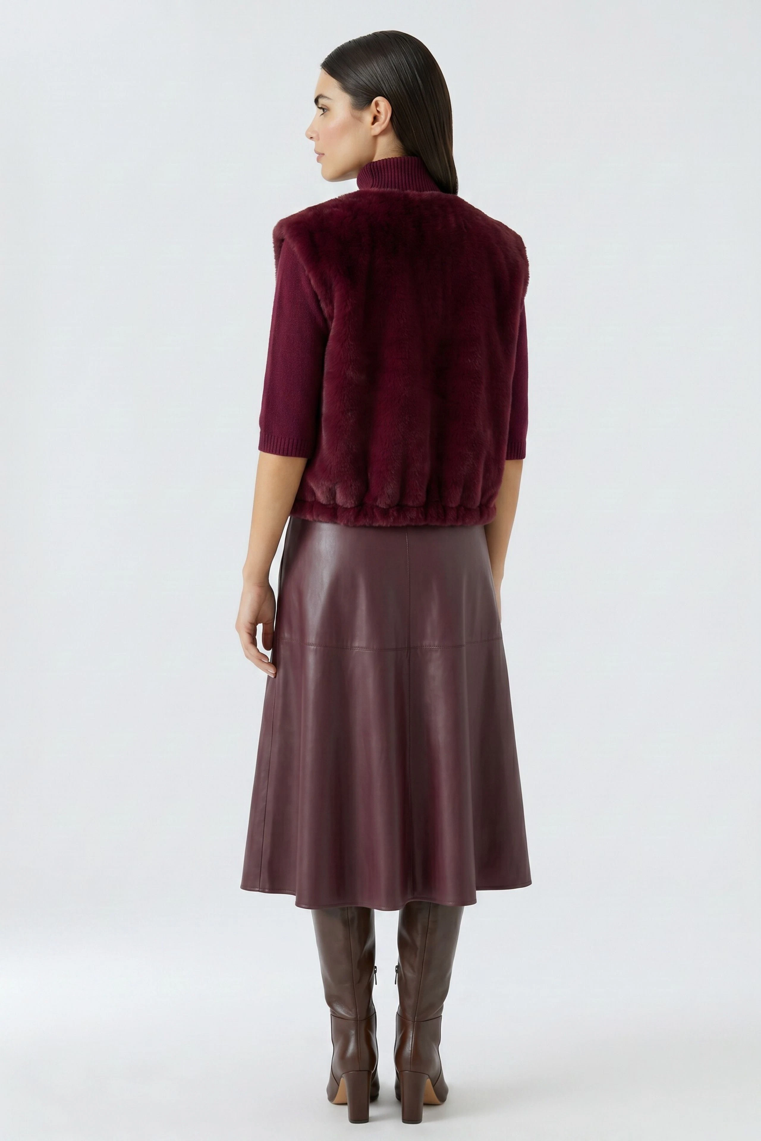 Woman in a burgundy vest, paired with a matching leather skirt and boots, showcasing a chic autumn look.