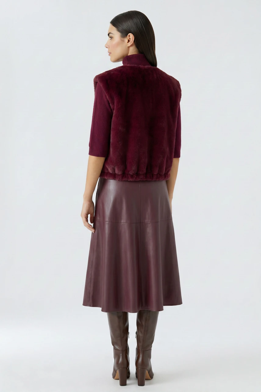 Woman in a burgundy vest, paired with a matching leather skirt and boots, showcasing a chic autumn look.