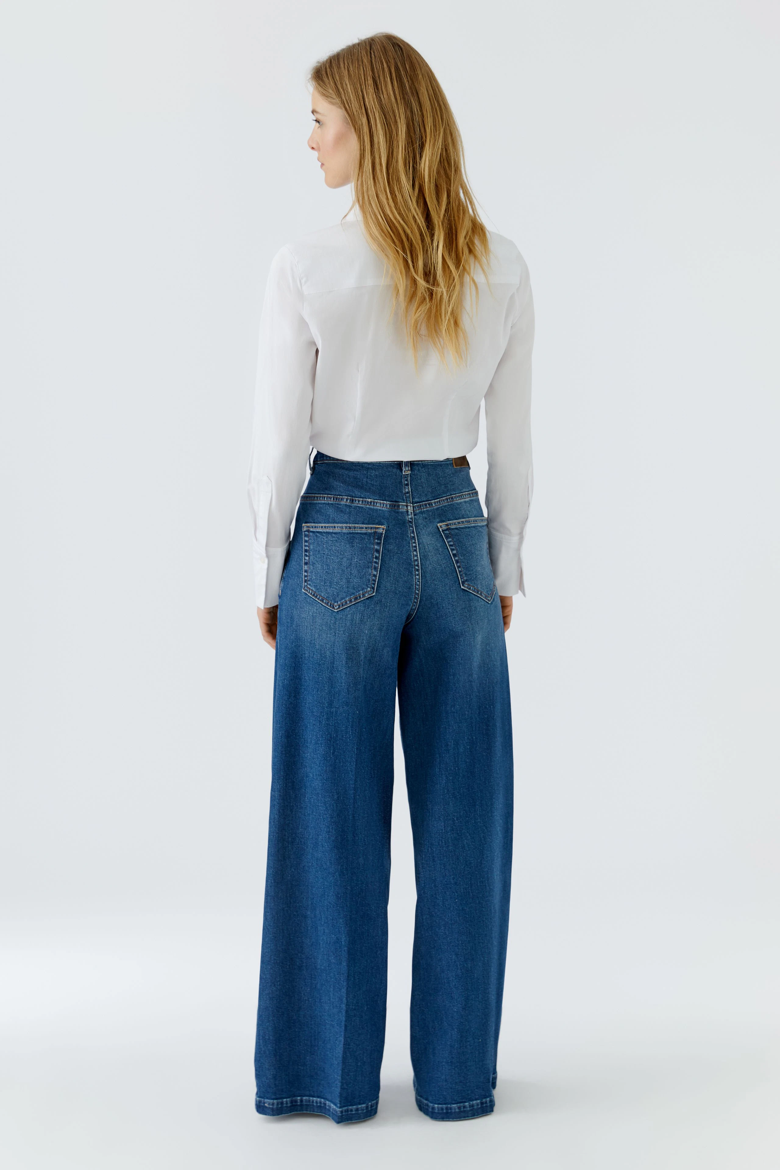 Woman in wide-leg jeans and white shirt, showcasing casual style from behind.
