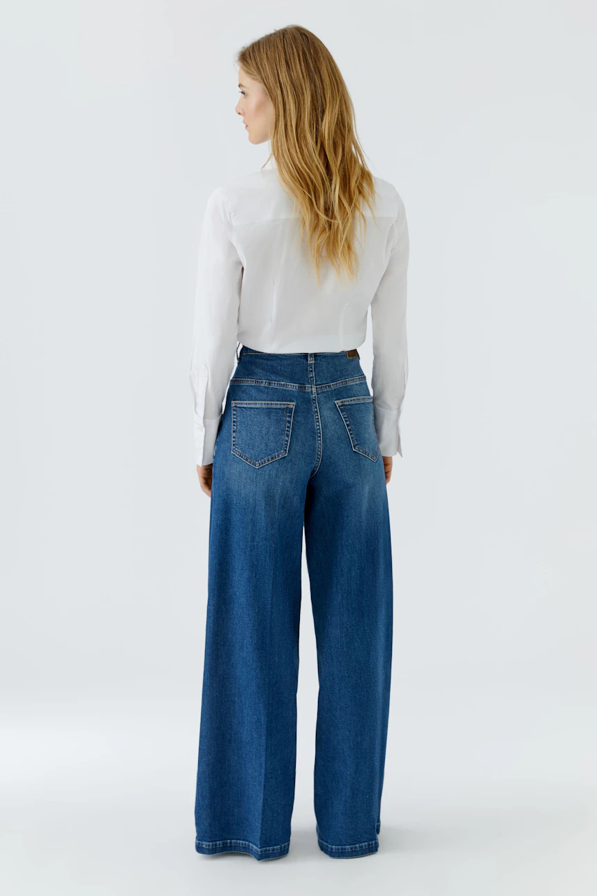 Frau in Jeans Wide Leg: Lässige Passform, kombiniert mit weißer Bluse, Rückansicht.