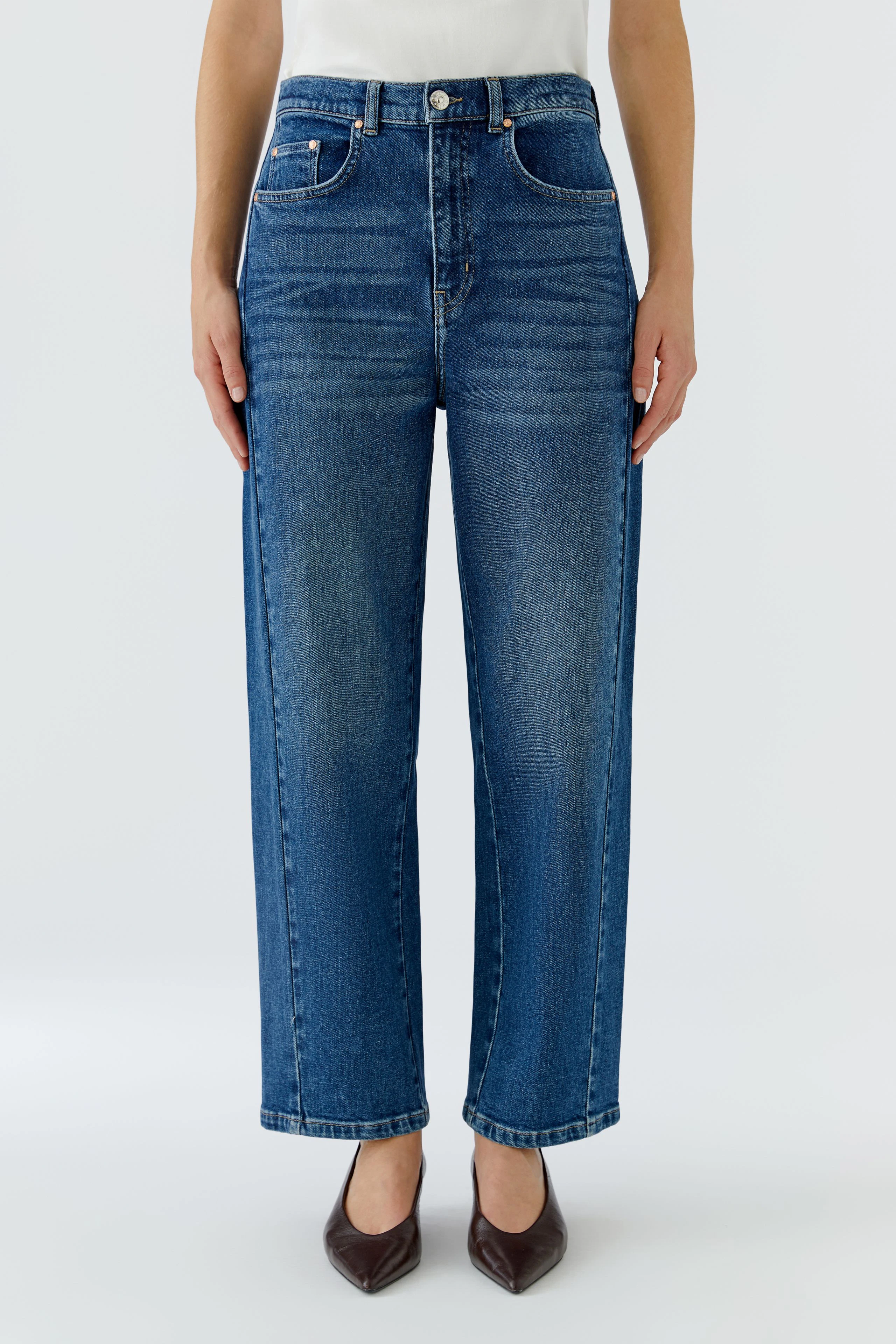 Woman in blue Barrel jeans, straight fit, high waist, paired with a white top, hands relaxed at sides.