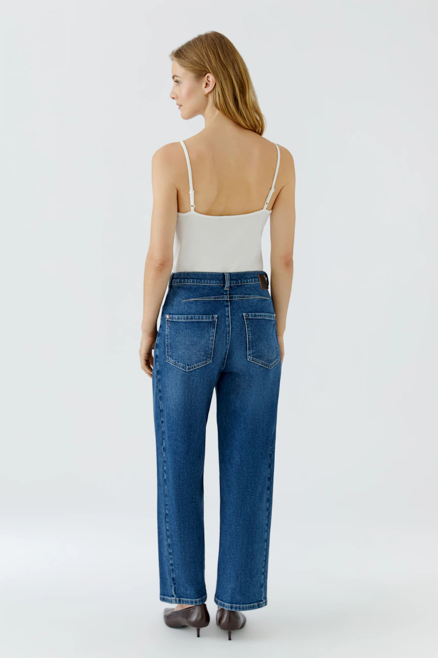Jeans Barrel: Frau in blauer Barrel-Jeans, Rückansicht, kombiniert mit weißem Top und Absatzschuhen.