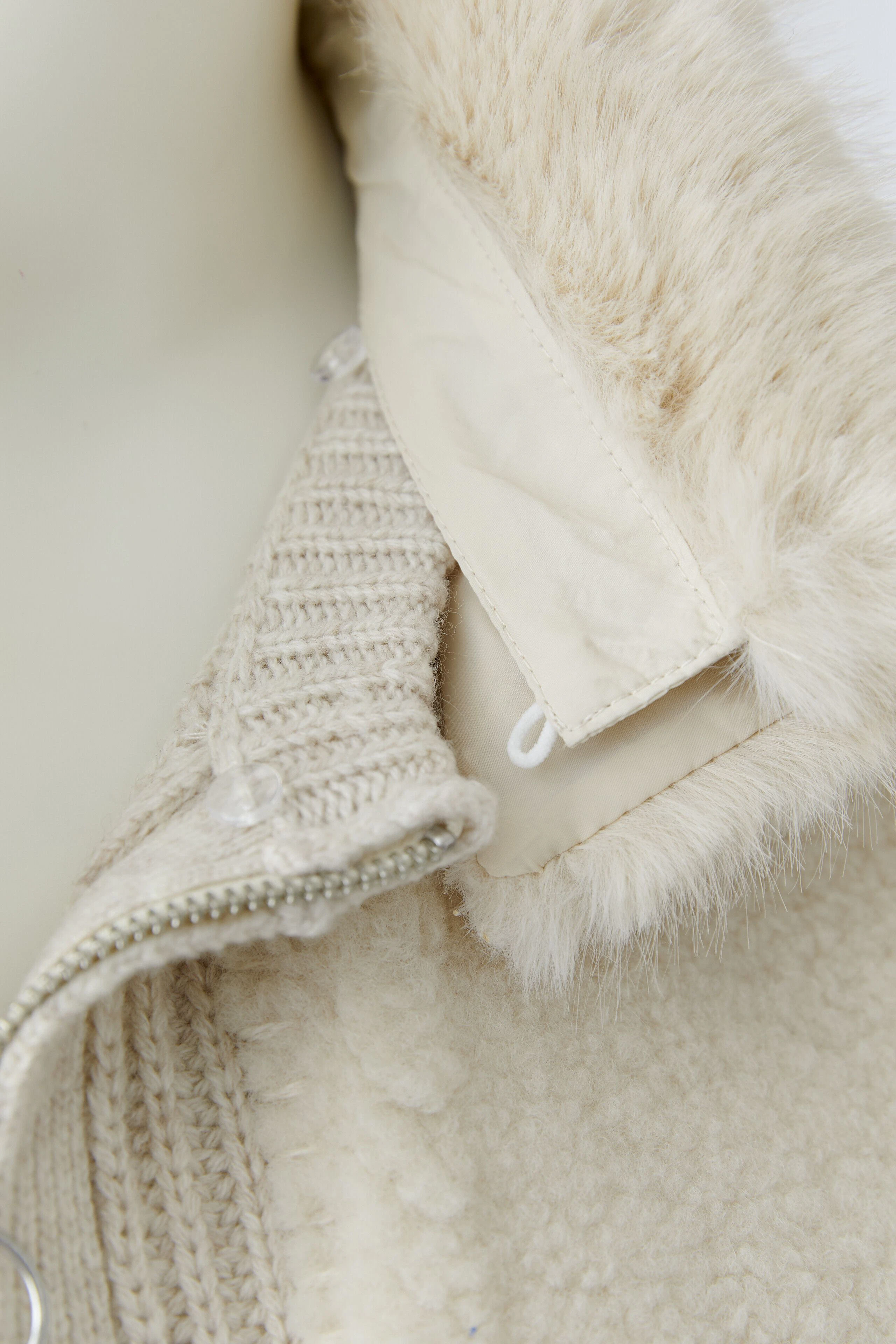 Strickjacke in Creme: Detailansicht des Kragens mit Reißverschluss und weichem Futter.