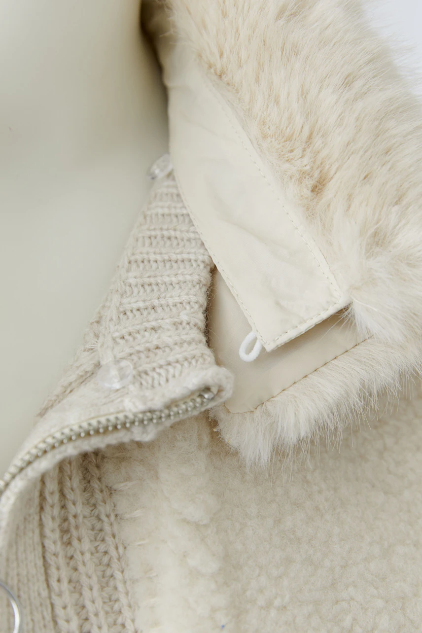 Strickjacke in Creme: Detailansicht des Kragens mit Reißverschluss und weichem Futter.