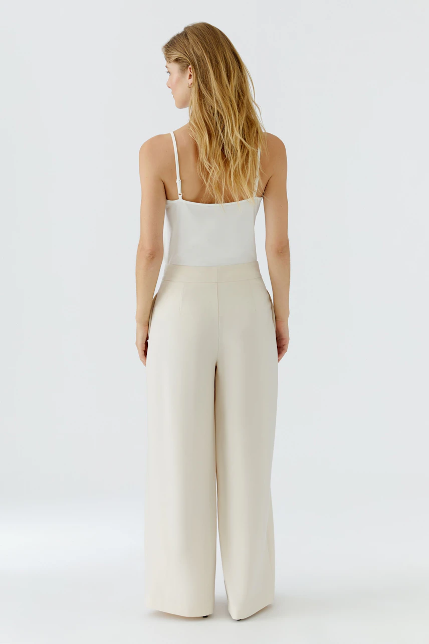 Woman in beige pleated trousers, white top, showcasing relaxed fit and style.