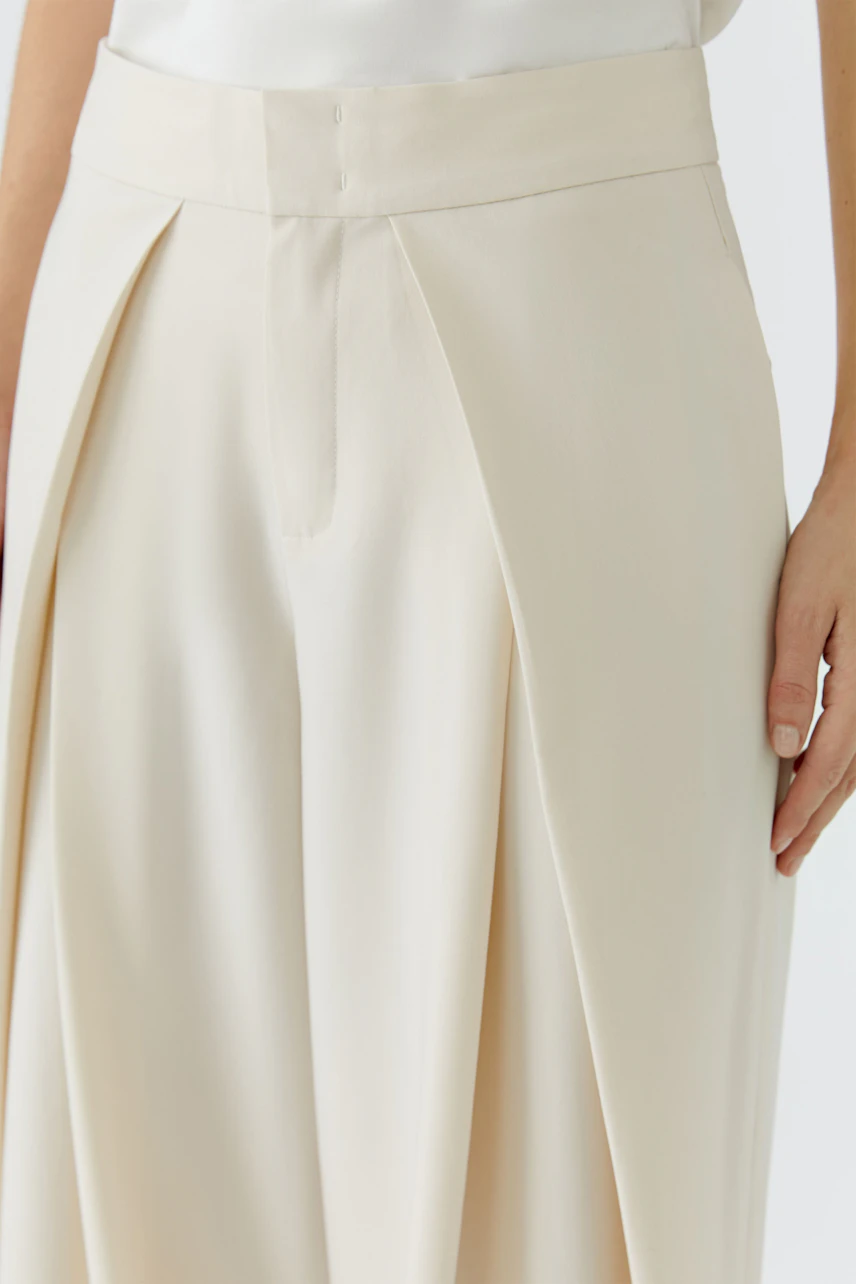 Woman in cream pleated trousers, showcasing a relaxed fit and high waist design.