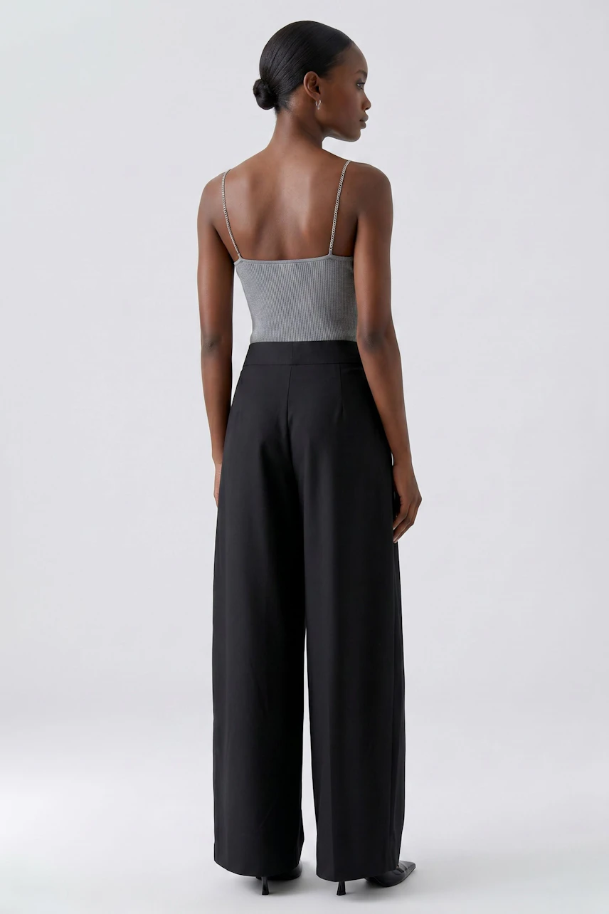 Woman in black pleated trousers and grey top, showcasing a stylish and relaxed look.