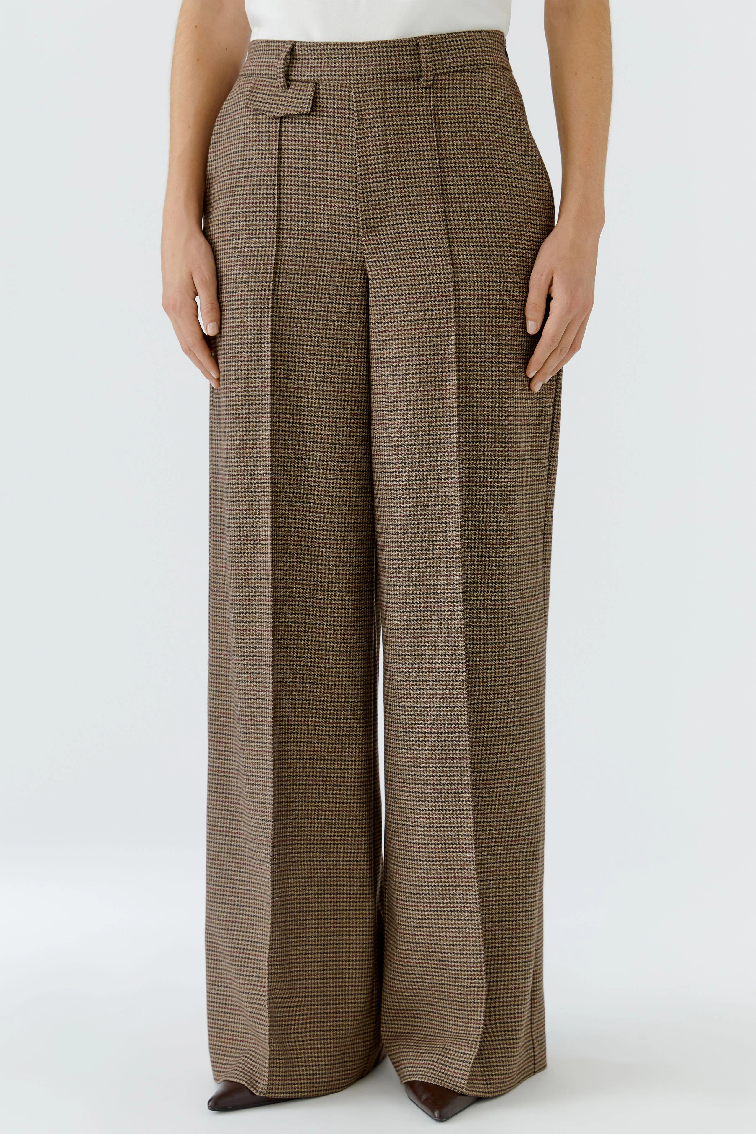 Woman in wide-leg trousers: Brown checkered pants with high waist and pleats, paired with a white top.