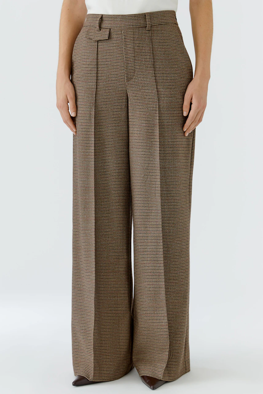 Woman in wide-leg trousers: Brown checkered pants with high waist and pleats, paired with a white top.