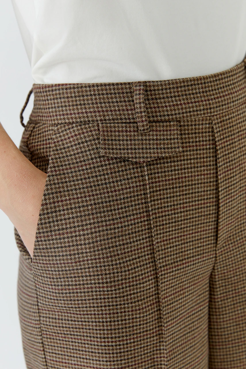 Casual women's pants: Close-up of brown checkered pants with side pockets, worn by a woman in a white top.