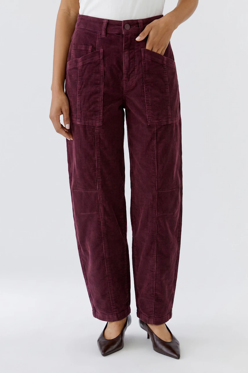 Casual women's pants: Woman in burgundy pants with large pockets, wearing a white top and brown shoes.