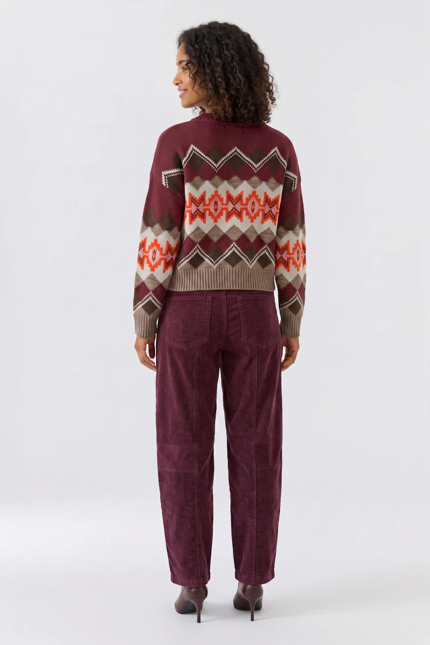 Casual women's pants: Woman in burgundy pants with a patterned pullover, standing confidently.