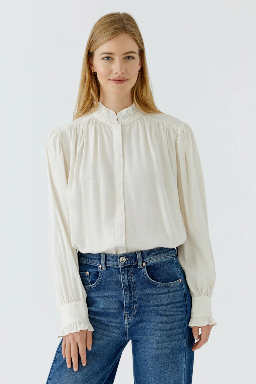 Casual women's blouse: Woman in a white blouse with ruffled cuffs and blue jeans, smiling confidently.
