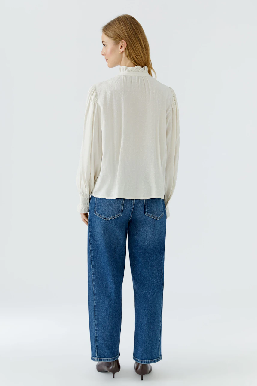 Casual blouse: Woman in a white blouse with long sleeves and relaxed fit, paired with blue jeans.