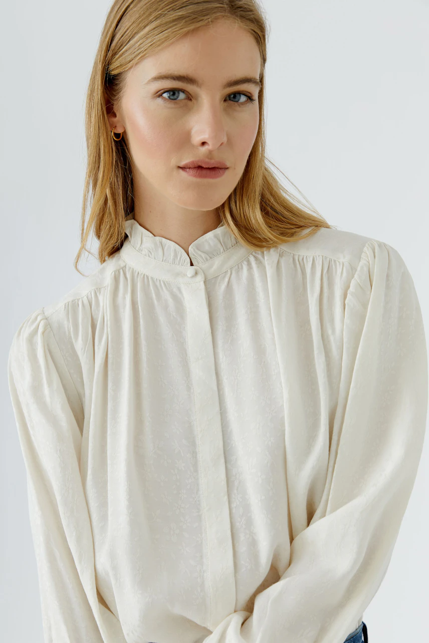 Woman in a white blouse with subtle texture, standing confidently. Simple and stylish design.