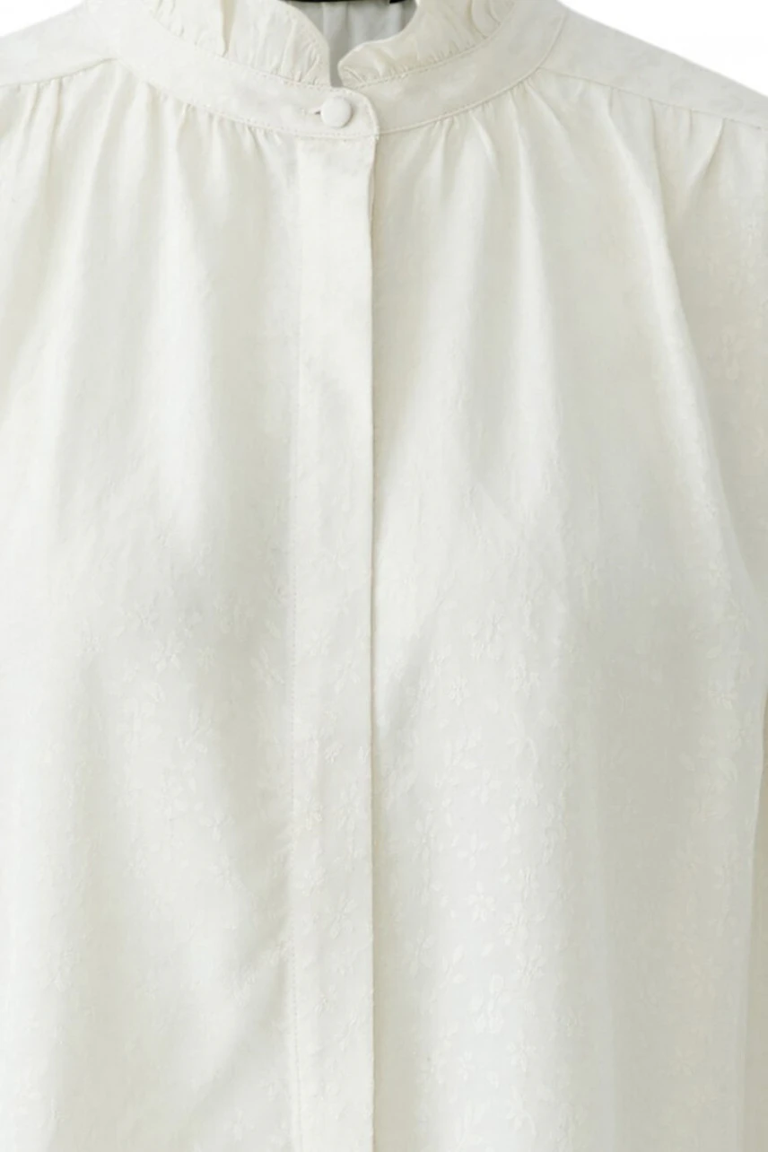 White blouse with subtle floral pattern, buttoned front, and high collar. No model shown.