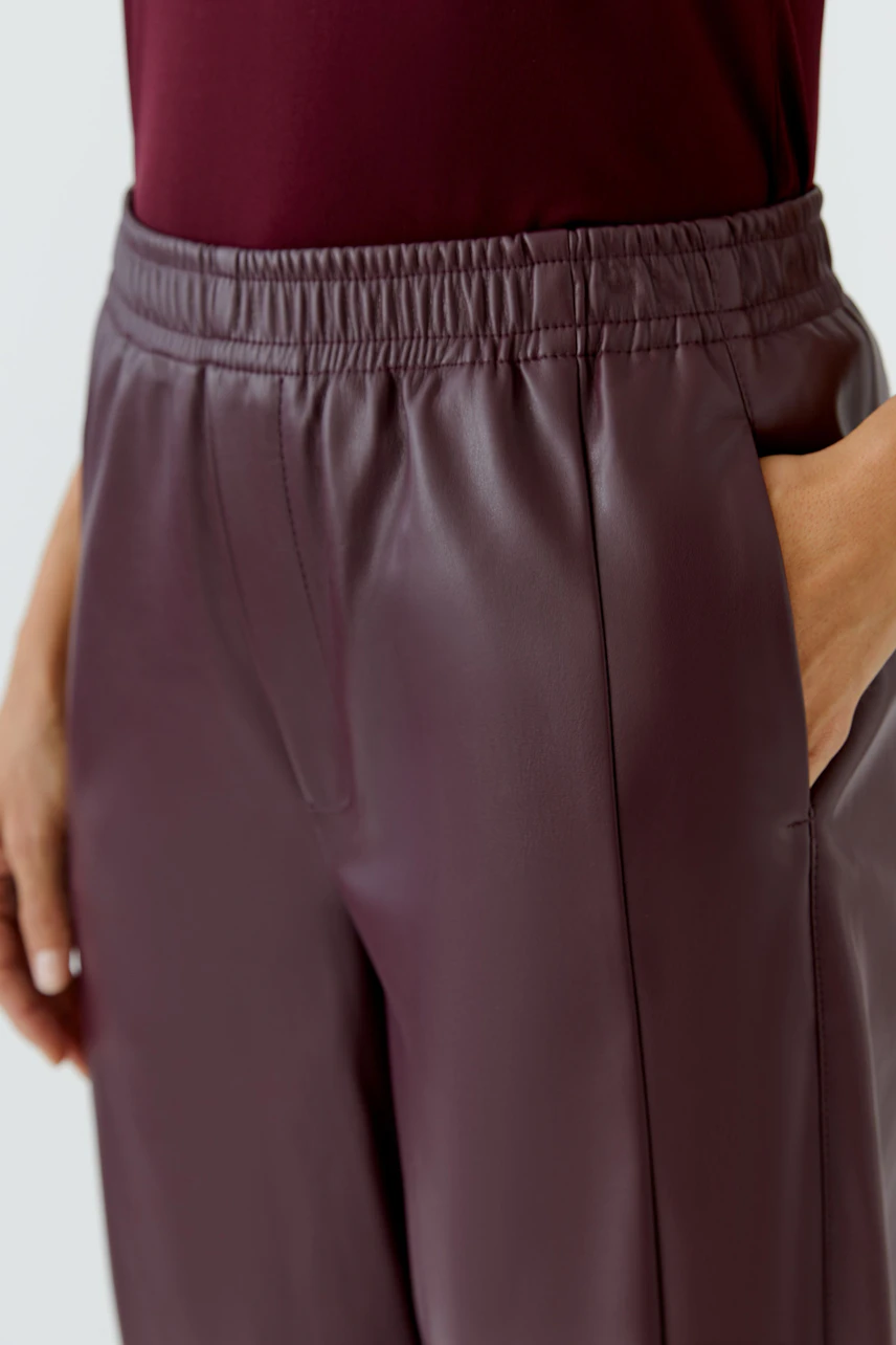 Lederimitathose: Frau in bordeauxfarbener Hose mit elastischem Bund und seitlichen Taschen.
