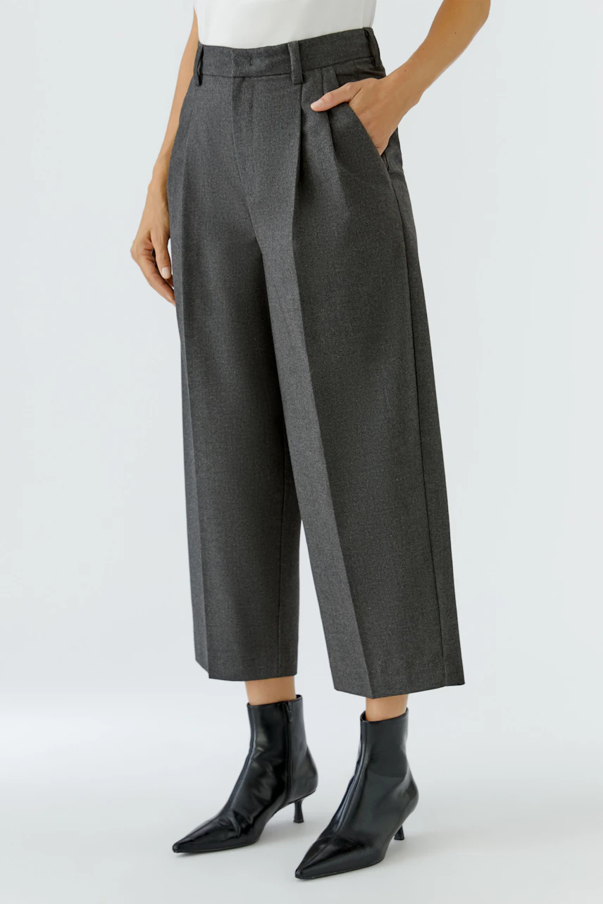 Frau in grauer Bundfaltenhose, kombiniert mit schwarzen Stiefeletten. Zeitloser Look für jeden Anlass.