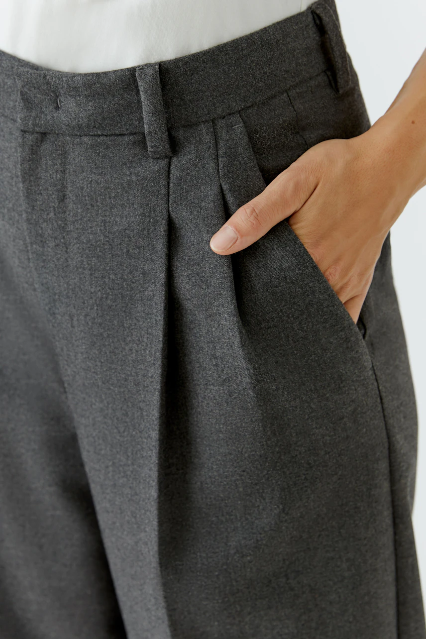 Graue Bundfaltenhose: Frau trägt lässige Hose mit seitlichen Taschen, kombiniert mit weißem Oberteil.