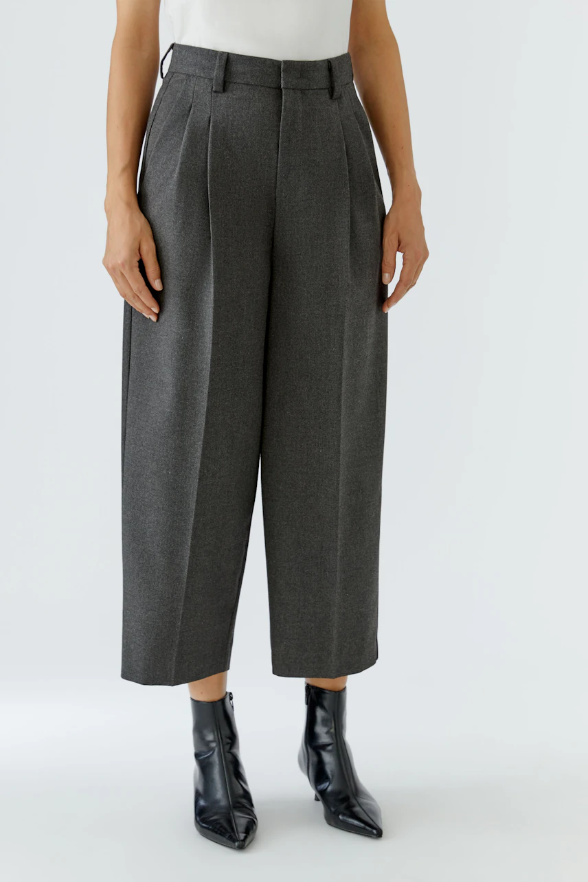 Frau in grauer Bundfaltenhose, kombiniert mit schwarzem Stiefel. Zeitloser Look für jeden Anlass.