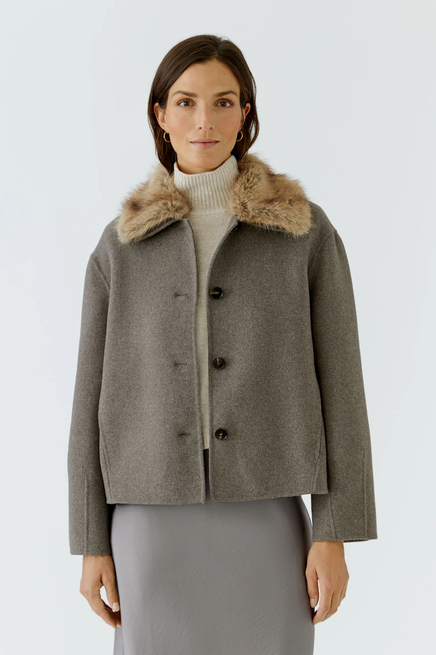 Damen-Jacke: Frau in grauer Jacke mit Fellkragen über Rollkragenpullover, schlicht und stilvoll.