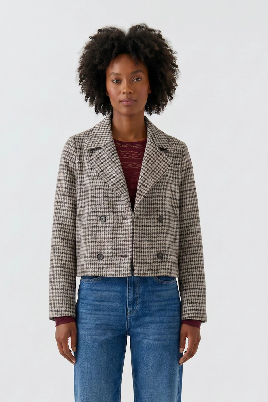 Casual women's jacket: Woman in a checkered jacket over a red top and blue jeans, standing confidently.