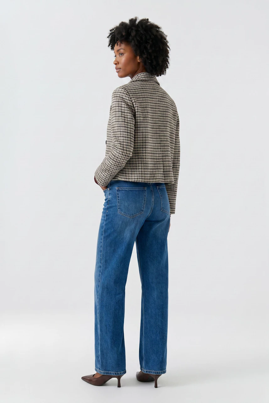 Casual jacket: Woman in a checkered jacket with blue jeans, standing confidently.