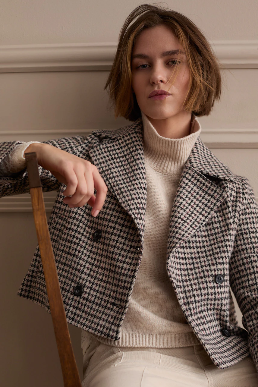 Woman in houndstooth jacket: Casual style with a cream turtleneck and relaxed pose.