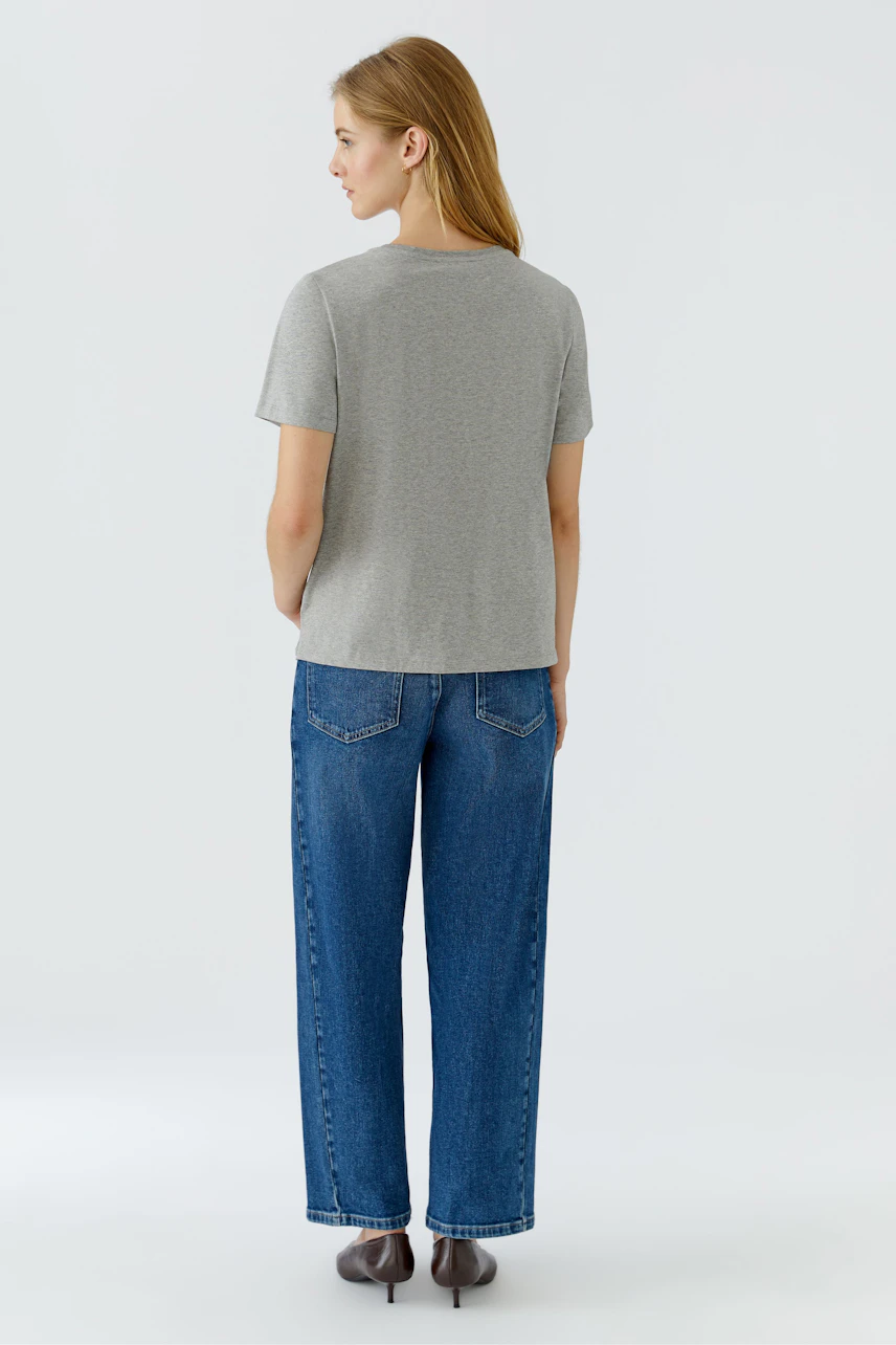 Casual women's T-shirt: Woman in a gray T-shirt and blue jeans, viewed from the back.