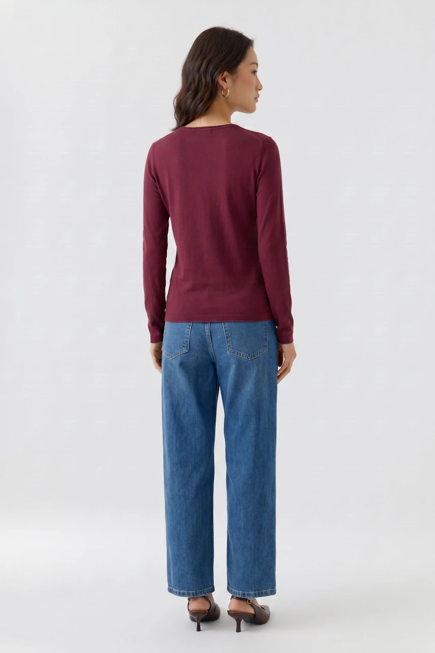 Frau im bequemen Langarmshirt in Bordeaux, kombiniert mit blauen Jeans, von hinten gesehen.