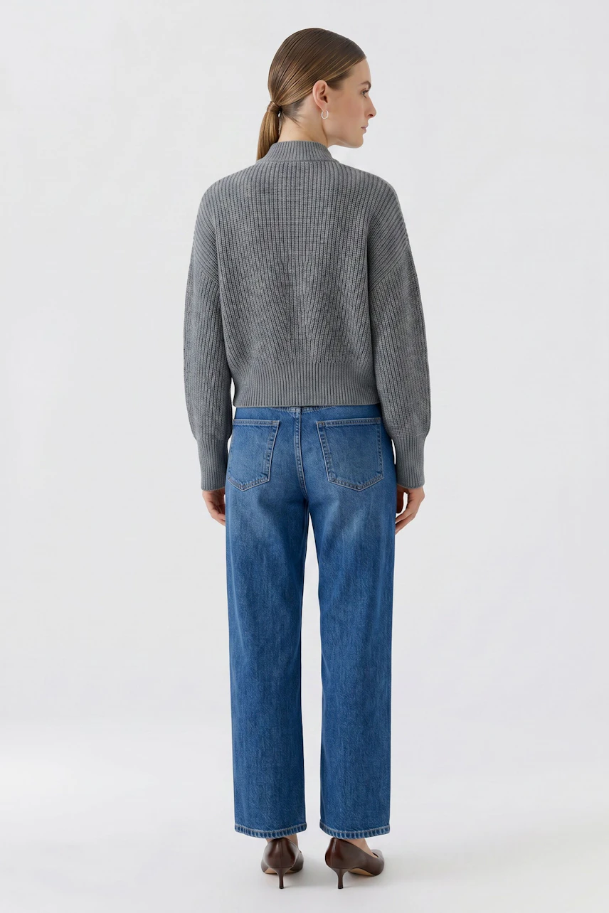Graue Strickjacke: Frau von hinten in grauer Strickjacke und blauer Jeans, schlicht und modern.
