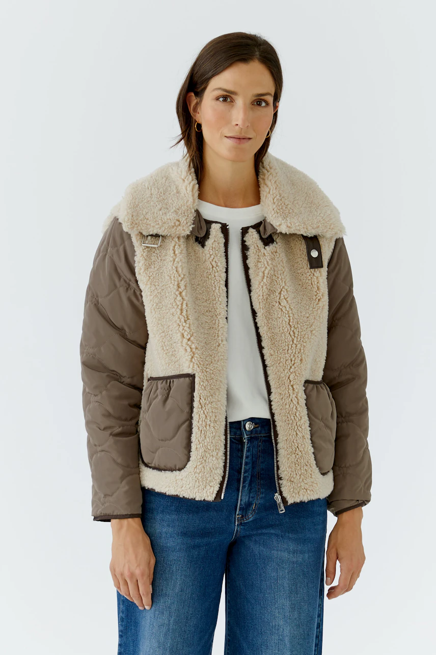 Casual outdoor jacket: Woman in a cozy, two-tone jacket with shearling details and quilted sleeves.