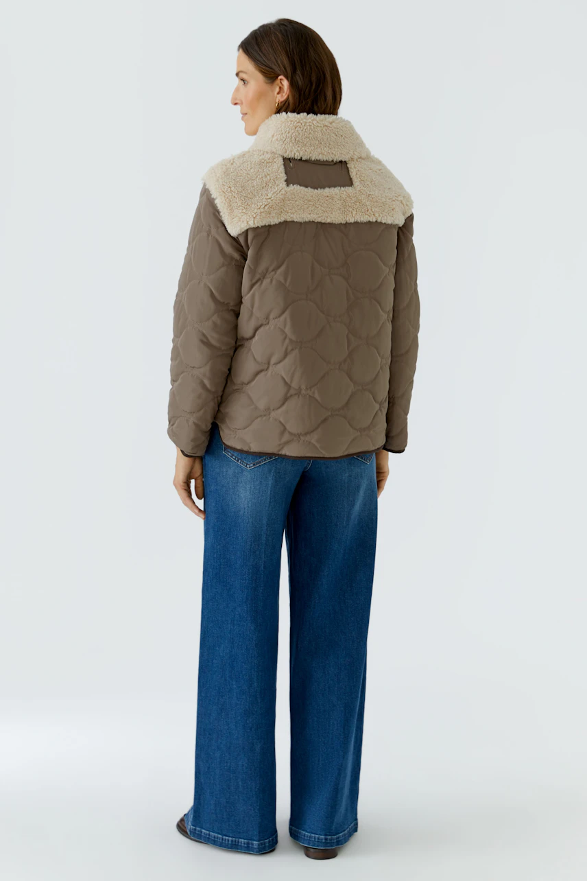 Casual outdoor jacket: Woman in quilted brown jacket with shearling collar, paired with wide-leg jeans.