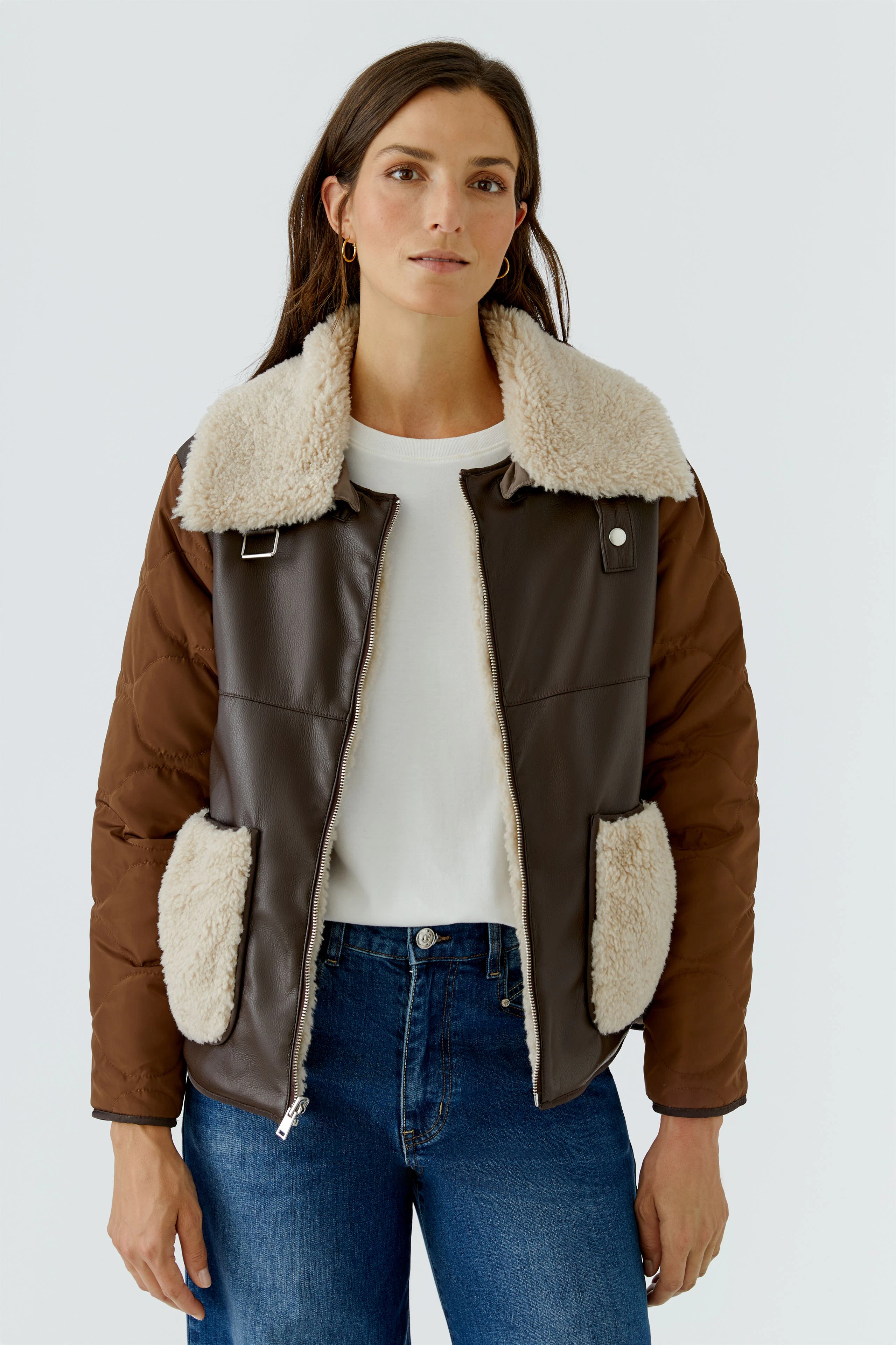Frau in brauner Outdoorjacke mit Fellkragen und Taschen, kombiniert mit weißem Shirt und blauen Jeans.
