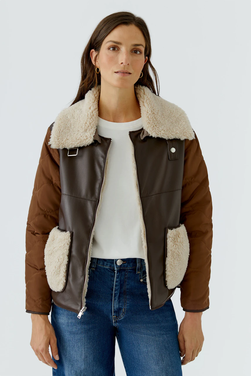 Woman in brown outdoor jacket with shearling collar, white tee, and jeans. Casual and warm look.