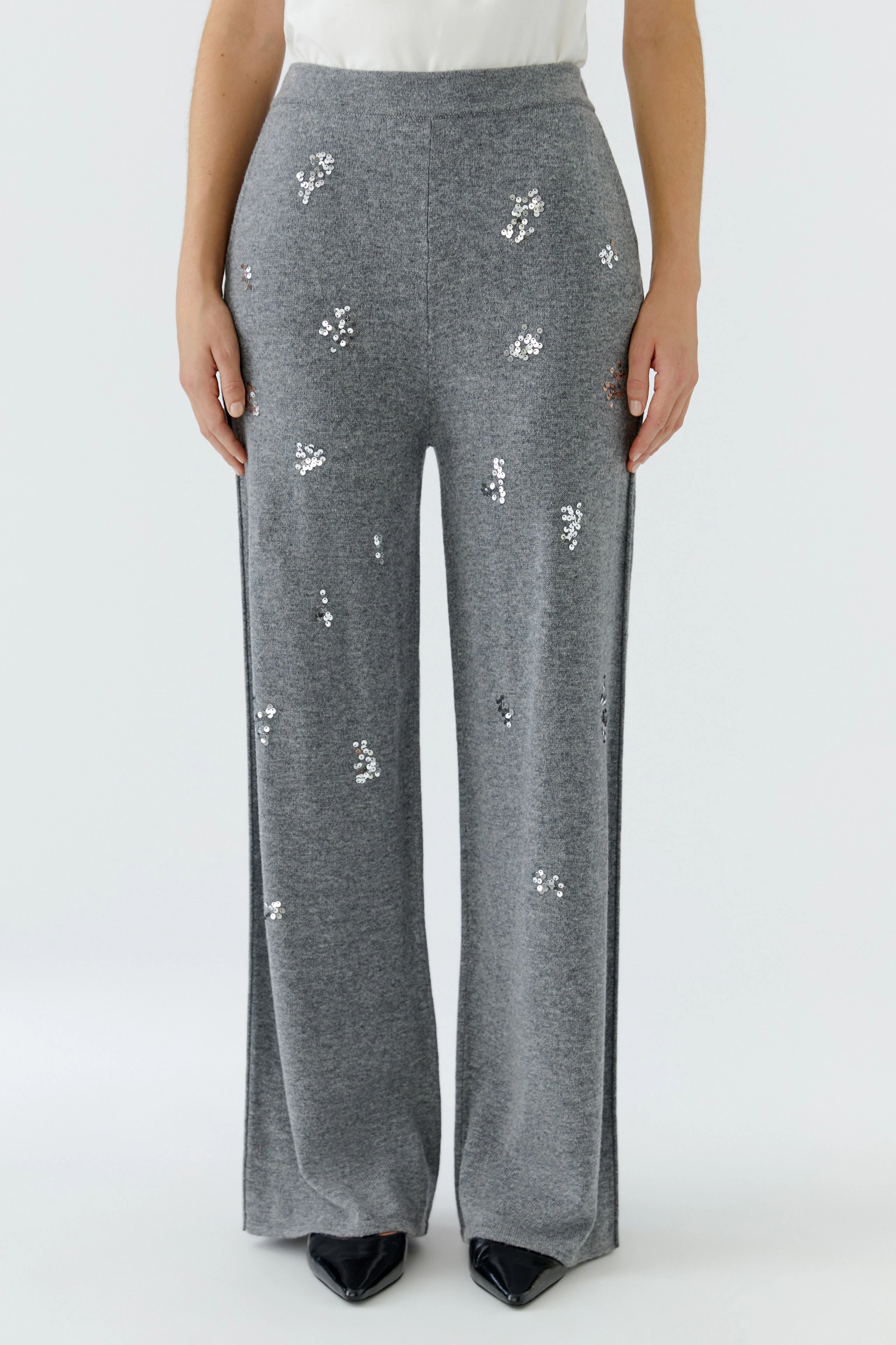 Woman in grey knit pants with subtle sequin details, paired with a white top, standing confidently.