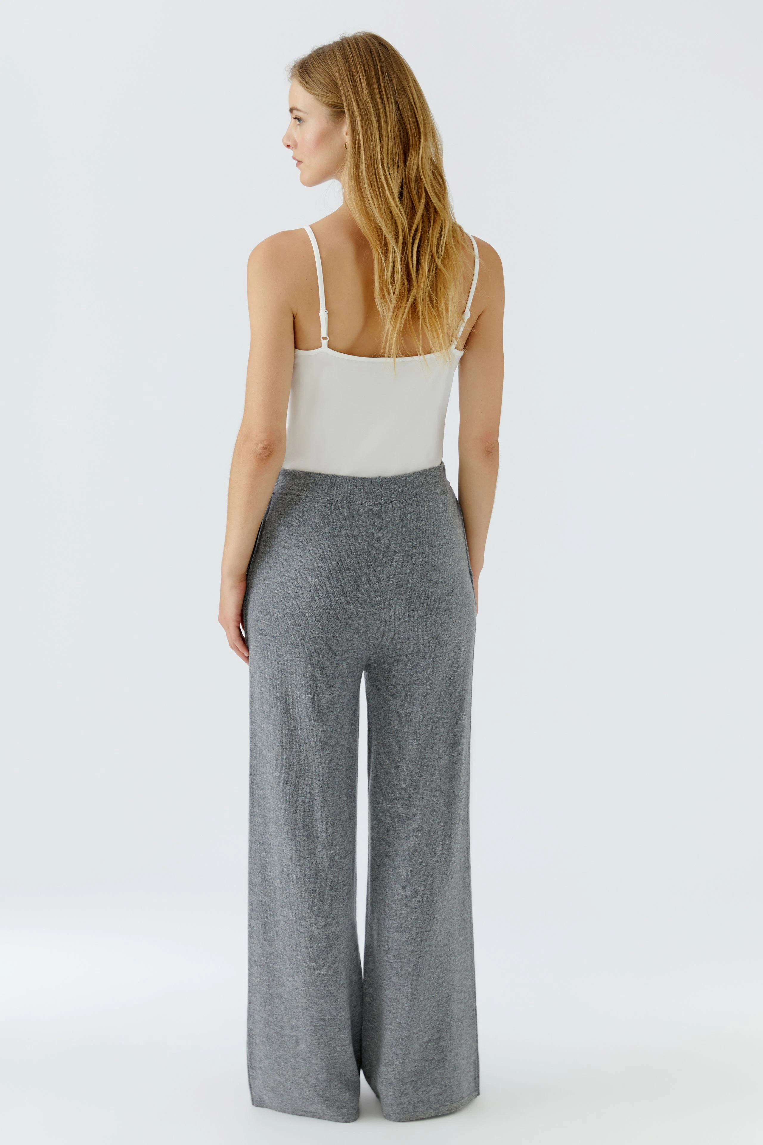 Woman in gray knit pants and white top, standing confidently. Casual and comfortable style.