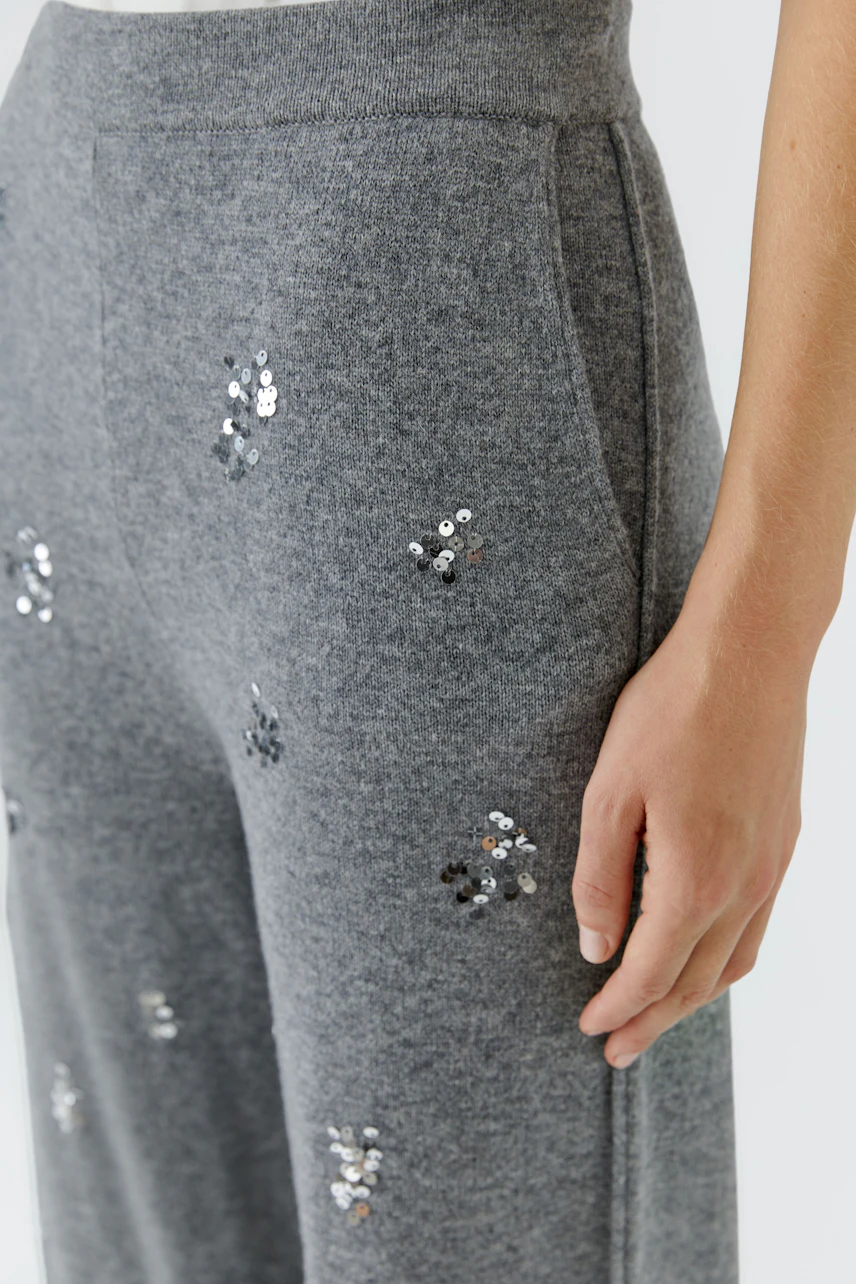 Graue Strickhose mit Pailletten: Frau trägt bequeme Hose mit funkelnden Details, ideal für lässige Outfits.