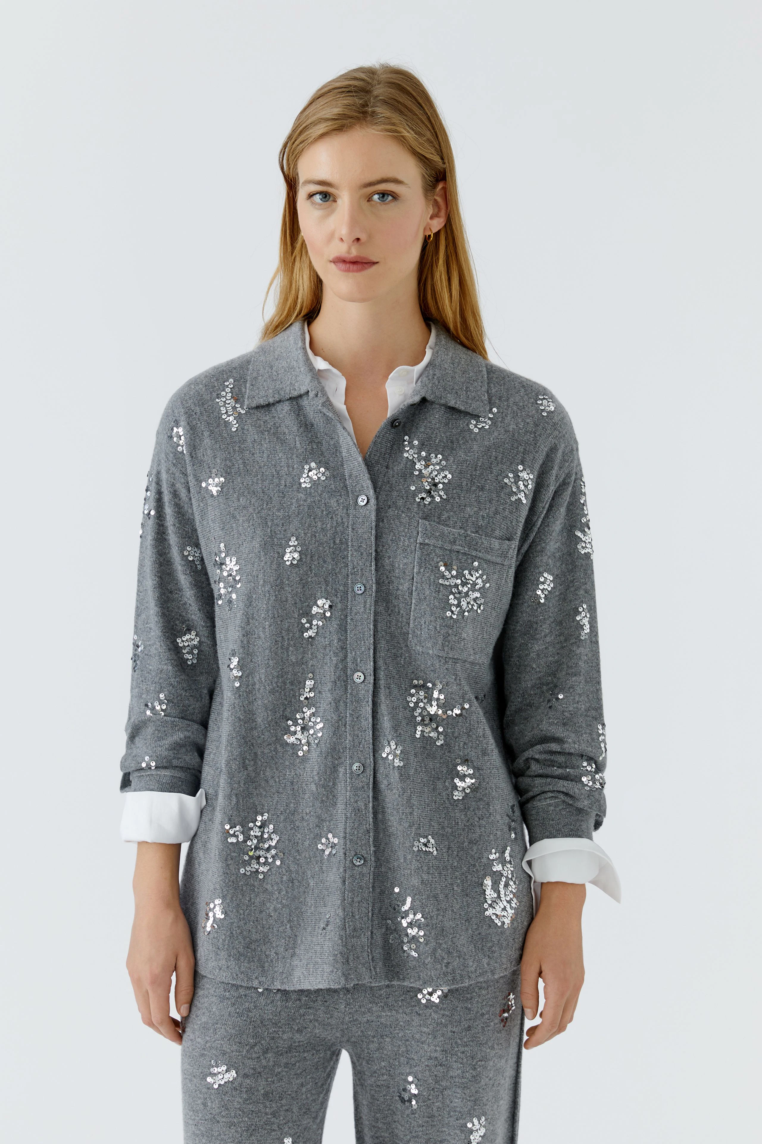 Graue Strickjacke: Frau trägt graue Strickjacke mit weißen Mustern, darunter weiße Bluse.