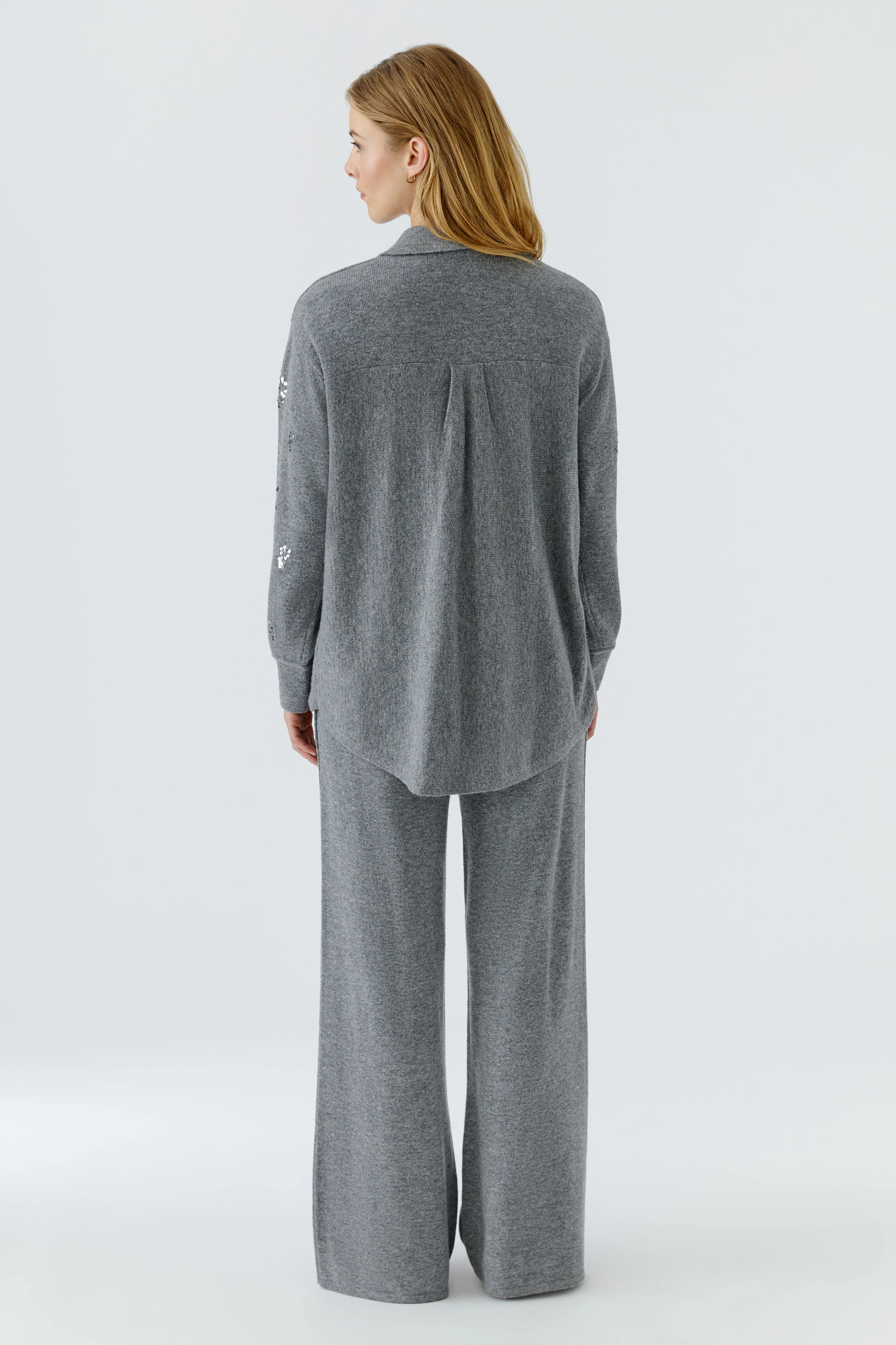 Graue Strickjacke: Frau von hinten in langer, grauer Strickjacke und passender Hose.