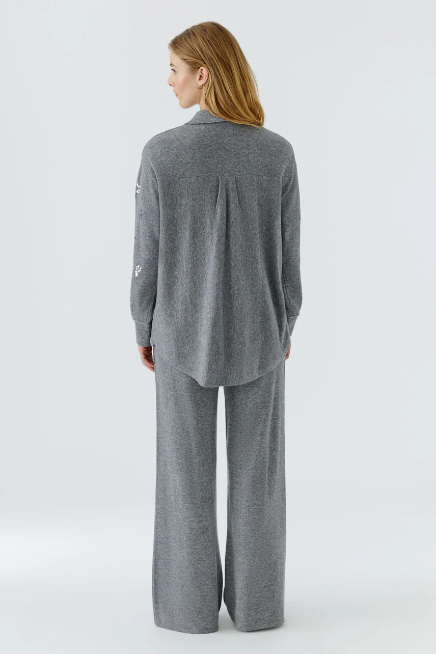 Graue Strickjacke: Frau von hinten in langer, grauer Strickjacke und passender Hose.