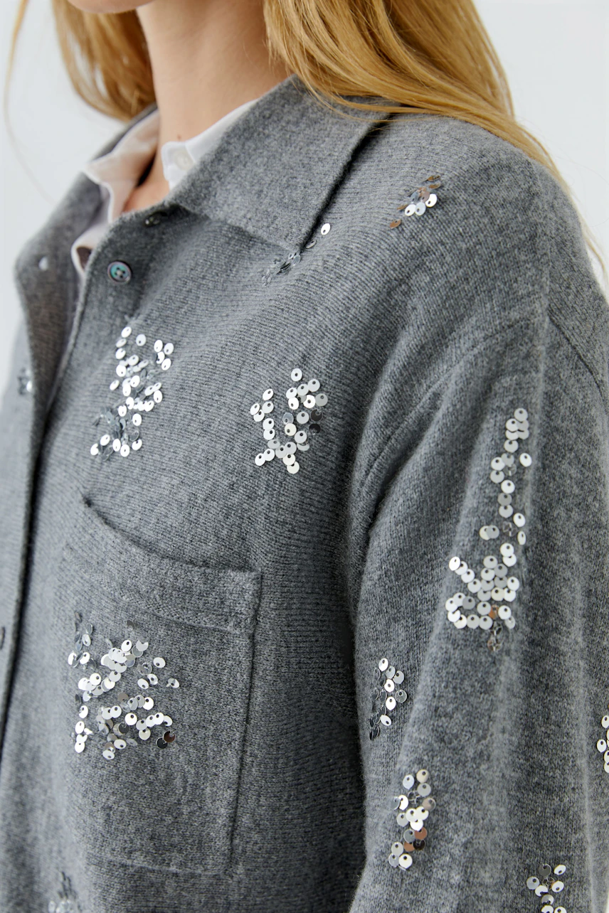 Graue Strickjacke mit Pailletten: Frau trägt lässige Jacke mit funkelnden Details und Hemd darunter.